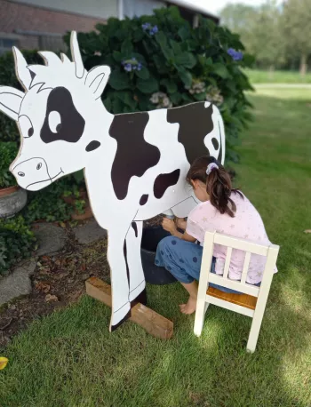 Kind dat oefent met melken aan een houten nepkoe tijdens een rondleiding