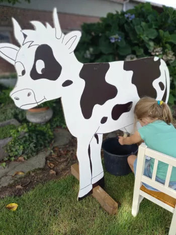 Kind dat oefent met melken aan een houten nepkoe tijdens een rondleiding